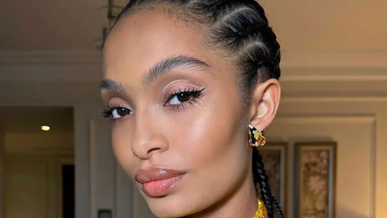 Primer plano de una mujer con trenzas, maquillaje de ojos con delineado y brillo, y labios brillantes.