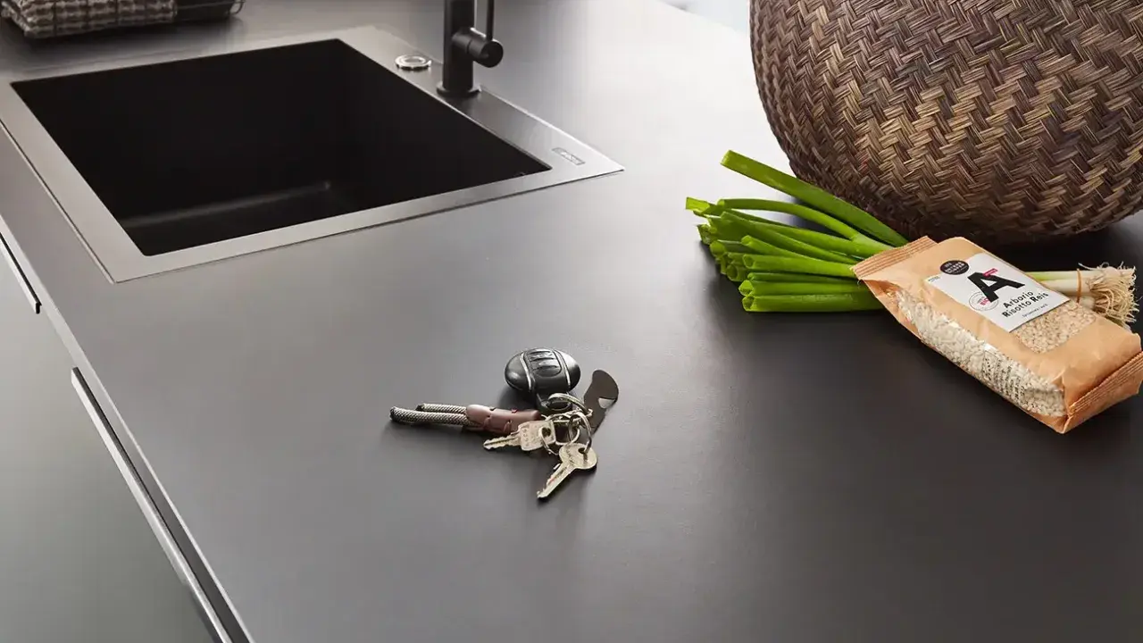 Dunkle Nobilia Arbeitsplatte mit Spüle, Schlüsselbund, Frühlingszwiebeln und Reis. Xtra Arbeitsplatte Nobilia Erfahrung: Praktisch und stilvoll.