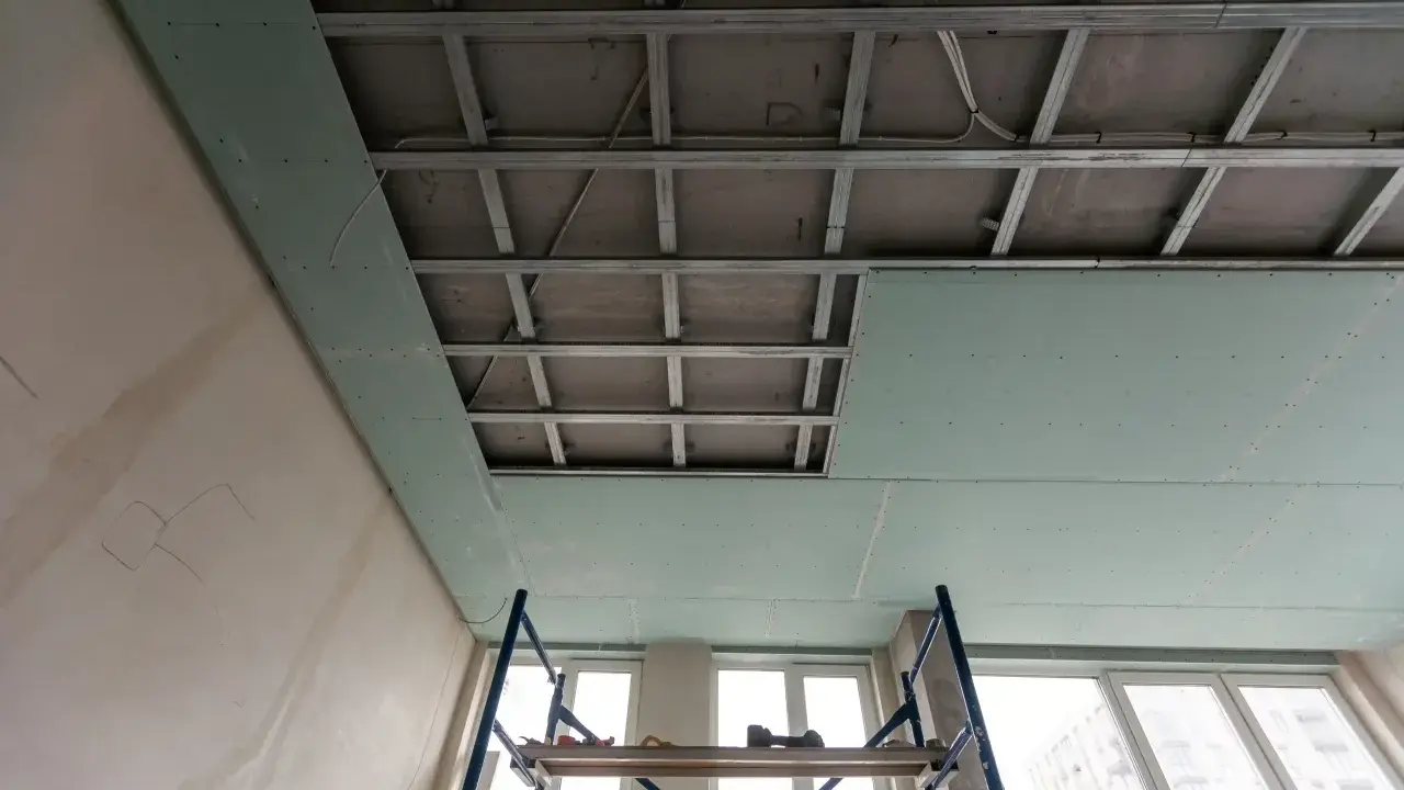 Instalación de falso techo de pladur para aislar techo ruido vecinos. Andamio y estructura metálica visibles.