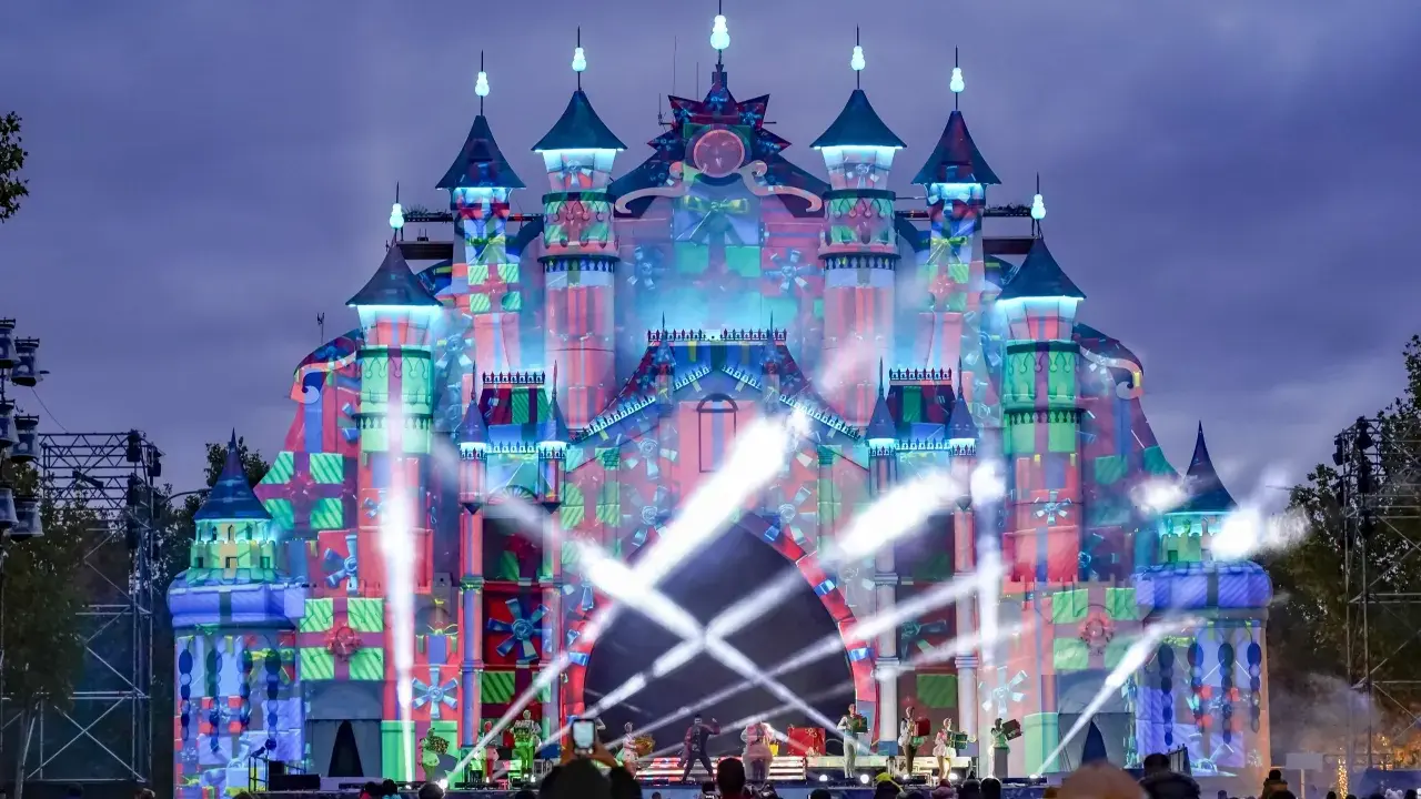 Castillo de luces y regalos en el parque navidad Torrejón. Artistas actúan en un escenario frente a la multitud.