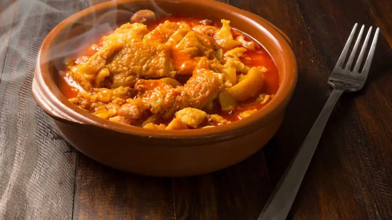 Un plat fumant de tête de veau mijotée, rappelant la recette tête de veau grand mère, servi dans un bol en terre cuite avec une fourchette.