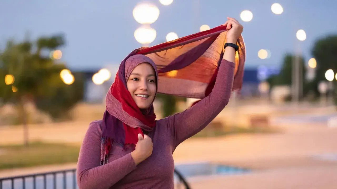 Lächelnde muslimische Frau mit buntem Hijab und Schal, der im Wind weht. Ein Bild, das die Vielfalt und Schönheit islamischer Kultur zeigt.