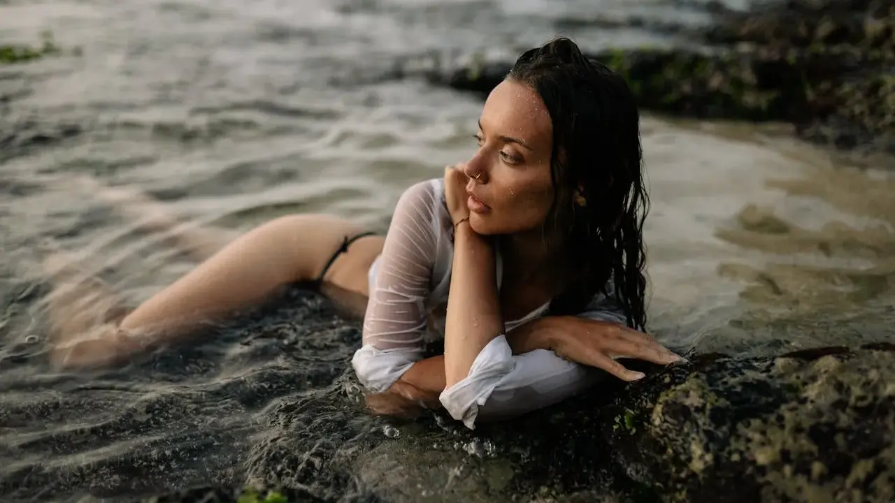 Modella in posa foto artistiche da fare al mare, sdraiata tra le rocce e l'acqua.