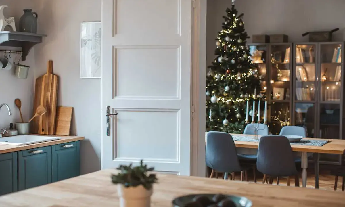 Julstämning i köket med en öppen dörr som avslöjar ett vackert julpyntat träd och en matsal. Perfekt jul inredning inspiration.