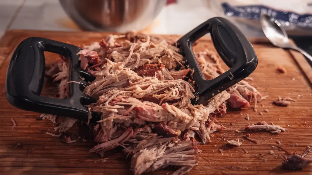 Pulled pork mit Fleischgabel auf Holzbrett. Perfekt für Smoker Rezepte Schwein, z.B. Pulled Pork Sandwiches.