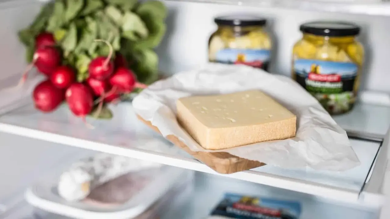 Ein Stück Käse liegt auf einem Holzbrett, daneben Radieschen und Gläser mit eingelegtem Gemüse. Verschiedene Käse sorten im Kühlschrank.