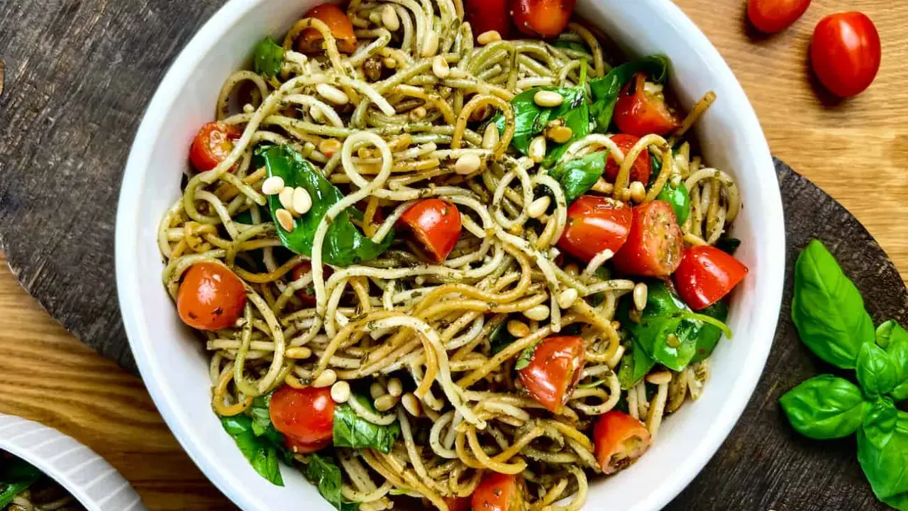 Leckerer Spaghetti-Salat zum Grillen mit Kirschtomaten, Pinienkernen und frischem Basilikum in einer weißen Schüssel.
