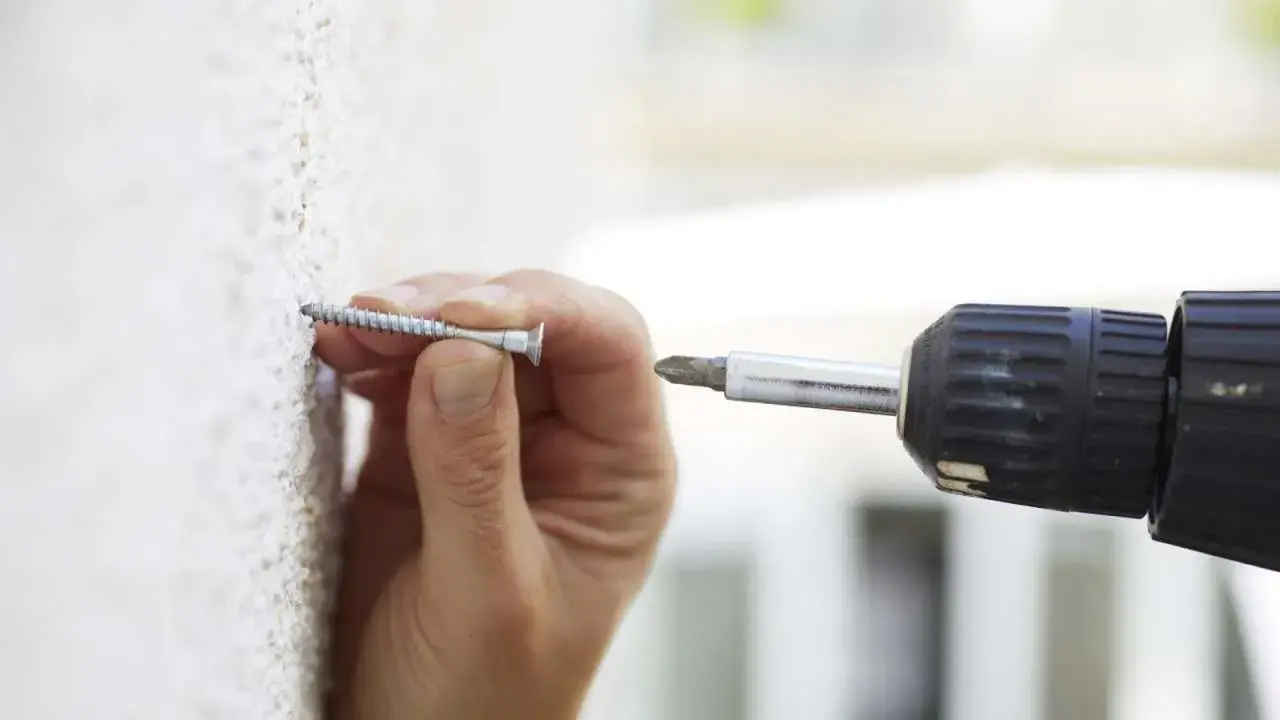 Mano insertando un tornillo en una pared texturizada, útil para saber si una pared es de pladur.