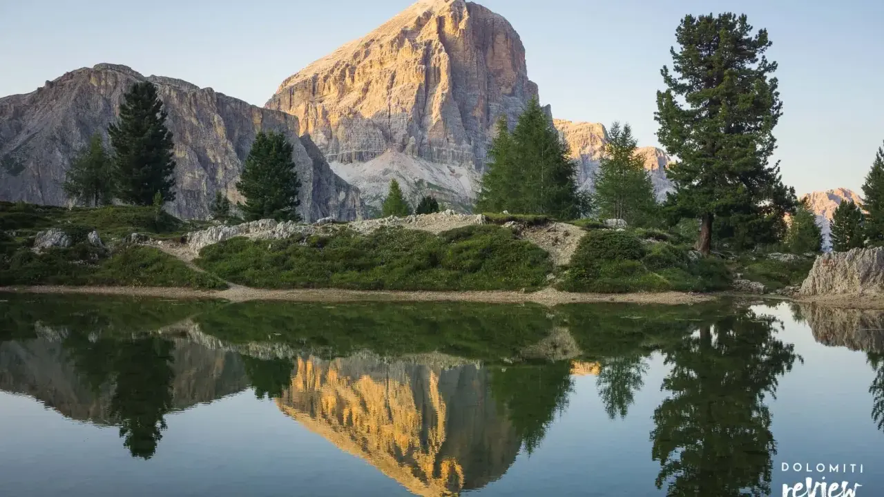 Riflesso perfetto di una montagna imponente nel lago di Limides, con alberi verdi e cielo azzurro.