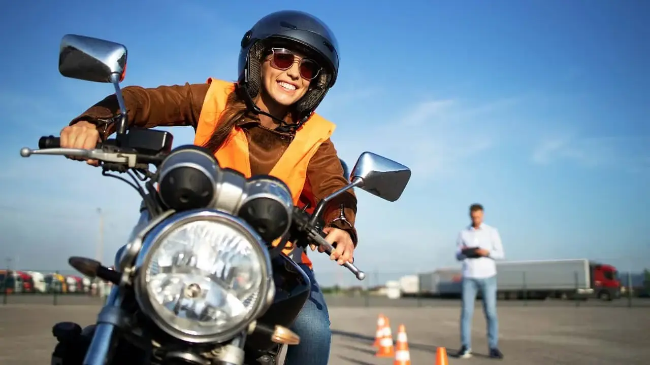 Uśmiechnięta kursantka na motorze, w kamizelce odblaskowej i kasku, uczy się jeździć. Zastanawiasz się, ile kosztują prawo jazdy na motor?