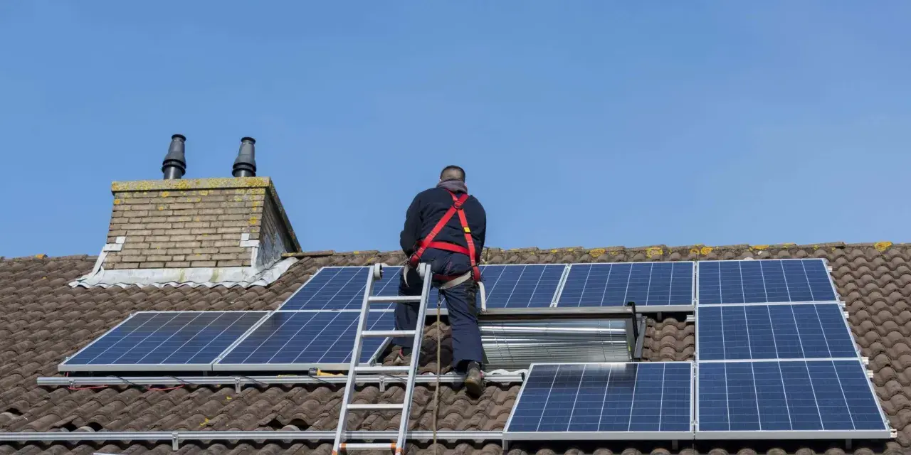 Un homme en harnais installe des panneaux solaires sur un toit. Un projet de panneau solaire installer soi-même en cours.