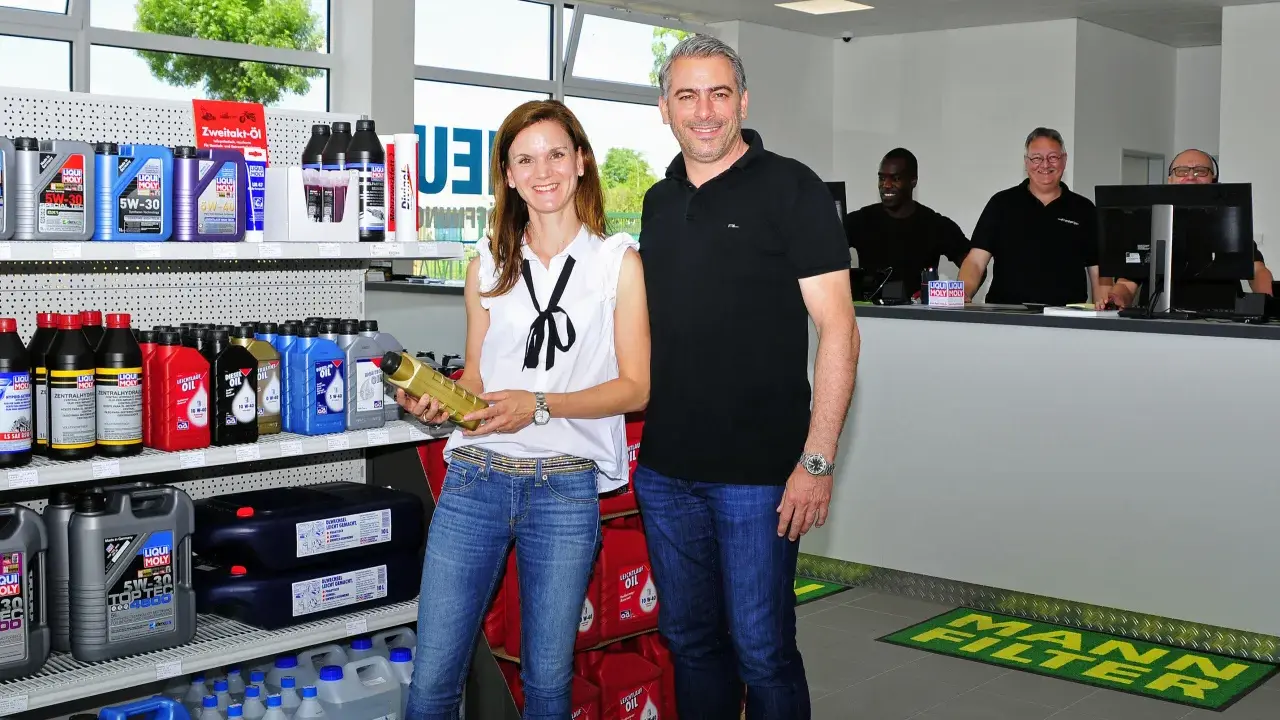 Ein Mann und eine Frau stehen vor Regalen mit Autoteilen und Ölflaschen.