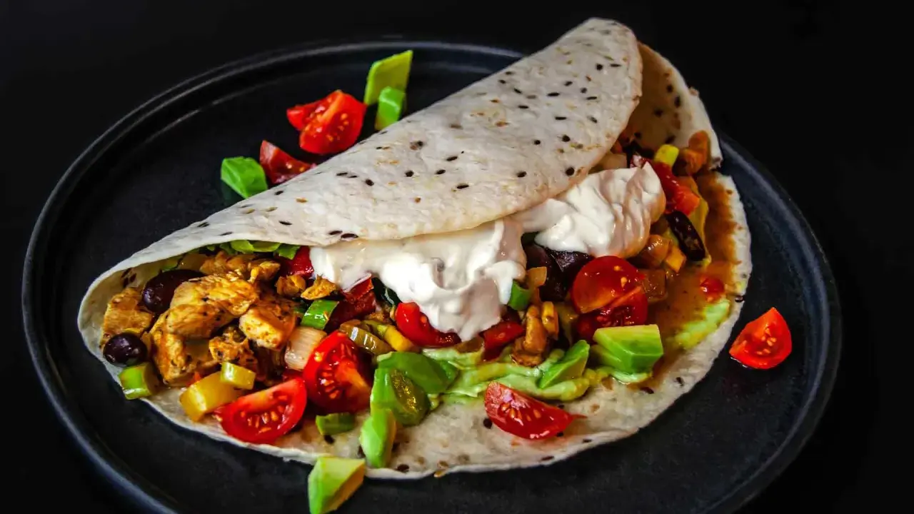 Ein köstliches Fajitas-Rezept: Tortilla gefüllt mit Hähnchen, Gemüse, Avocado und Sour Cream, garniert mit Tomaten.