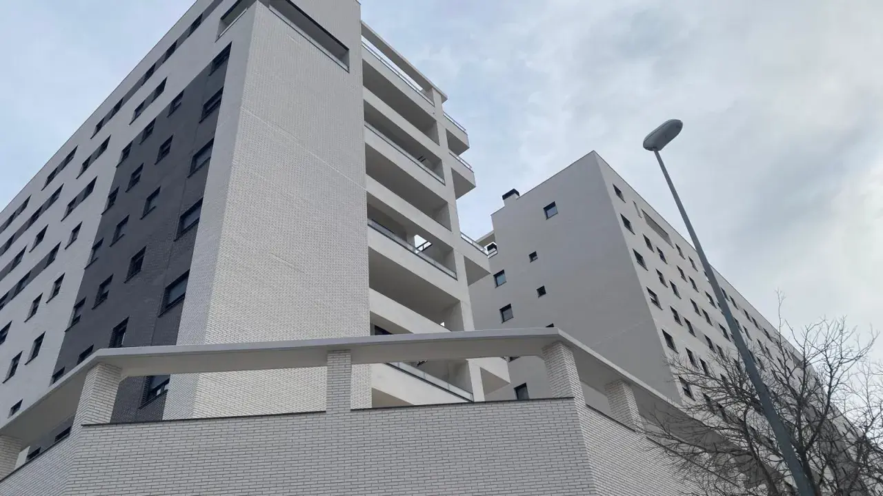 Modernas viviendas VPO en Alicante, edificios de ladrillo blanco y gris con balcones, bajo un cielo nublado.
