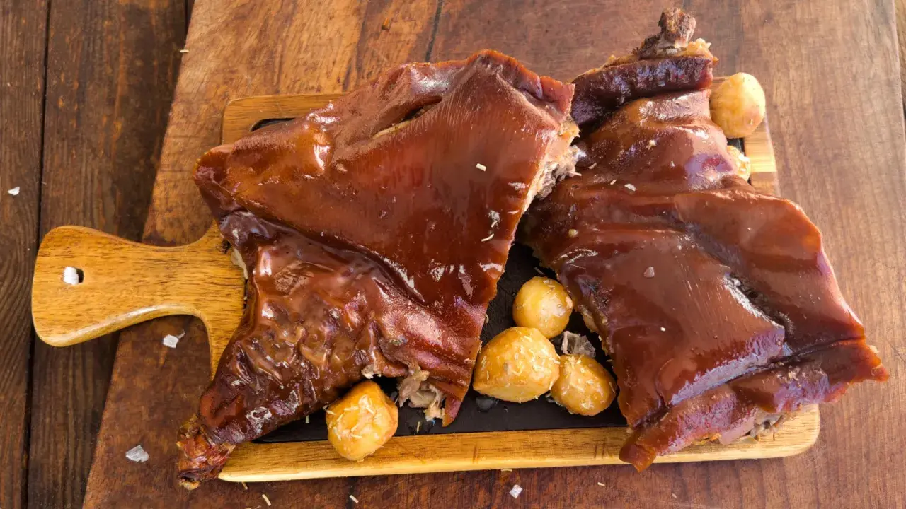 Delicioso cochinillo al horno, crujiente y jugoso, servido con patatas asadas sobre tabla de madera.