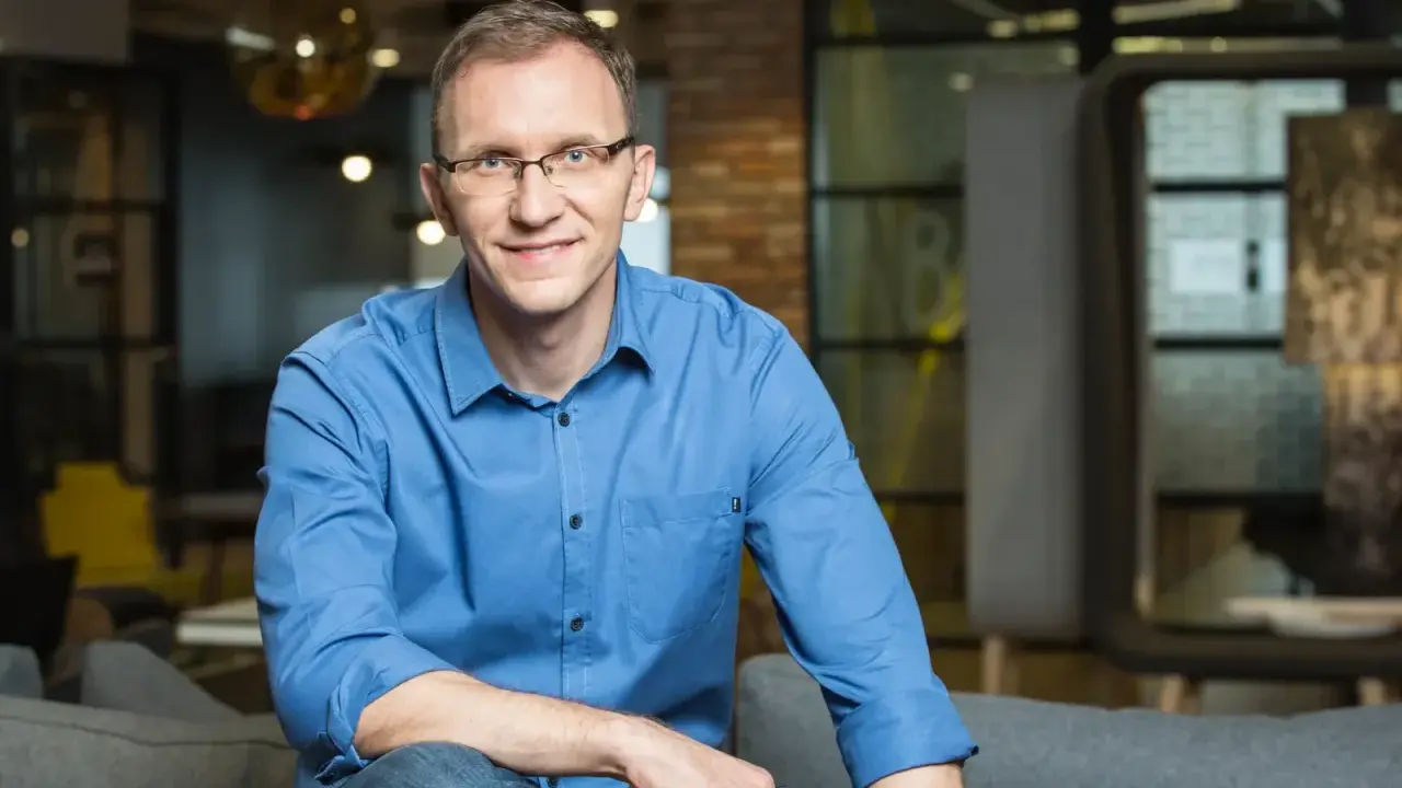 Marcin Iwuć, twórca "Finansowej fortecy", w niebieskiej koszuli siedzi na kanapie, uśmiechając się do obiektywu.