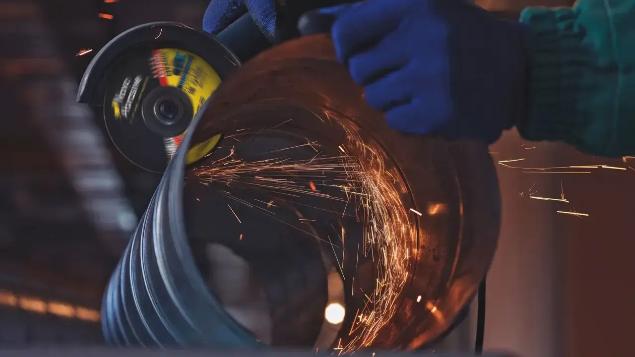 Manos enguantadas usan una radial para cortar un tubo, generando chispas. Un accidente con radial es un riesgo constante.
