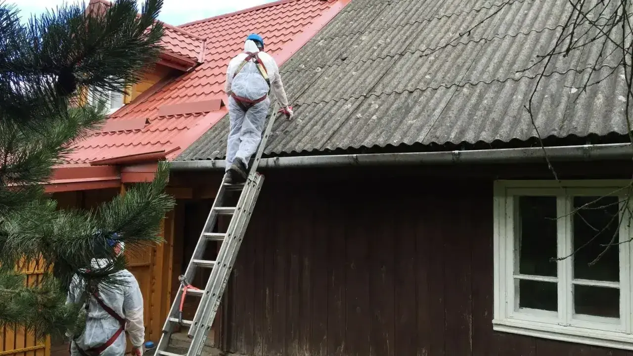 Pracownicy w kombinezonach zabezpieczających usuwają eternit z dachu. To pokazuje, co to jest azbest i jak wygląda jego utylizacja.