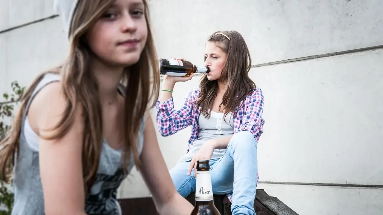 Dwie nastolatki piją piwo, co może być początkiem alkoholizmu wśród młodzieży.