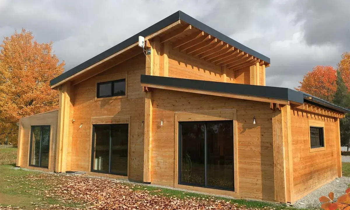 Une belle maison en bois, prête à accueillir ses habitants. L'automne arrive, les feuilles tombent autour de cette construction chaleureuse.