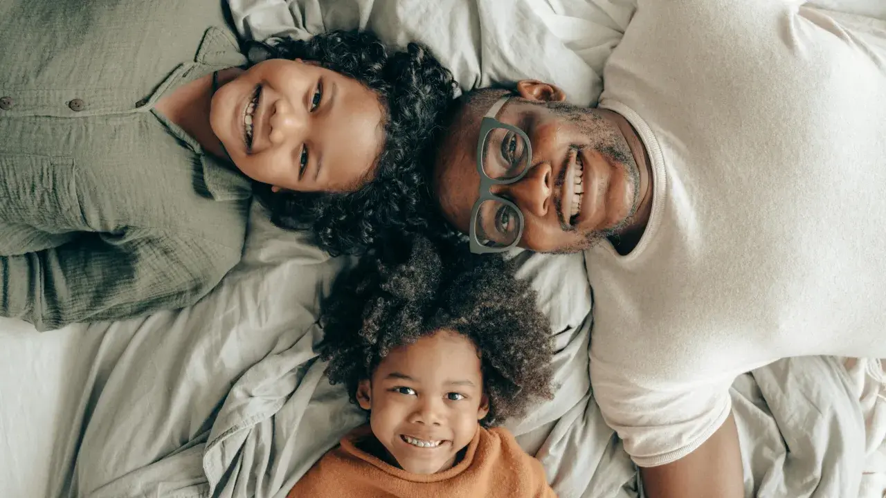 Un padre e i suoi due figli sorridono sdraiati sul letto, creando delle foto di famiglia originali e piene d'amore.