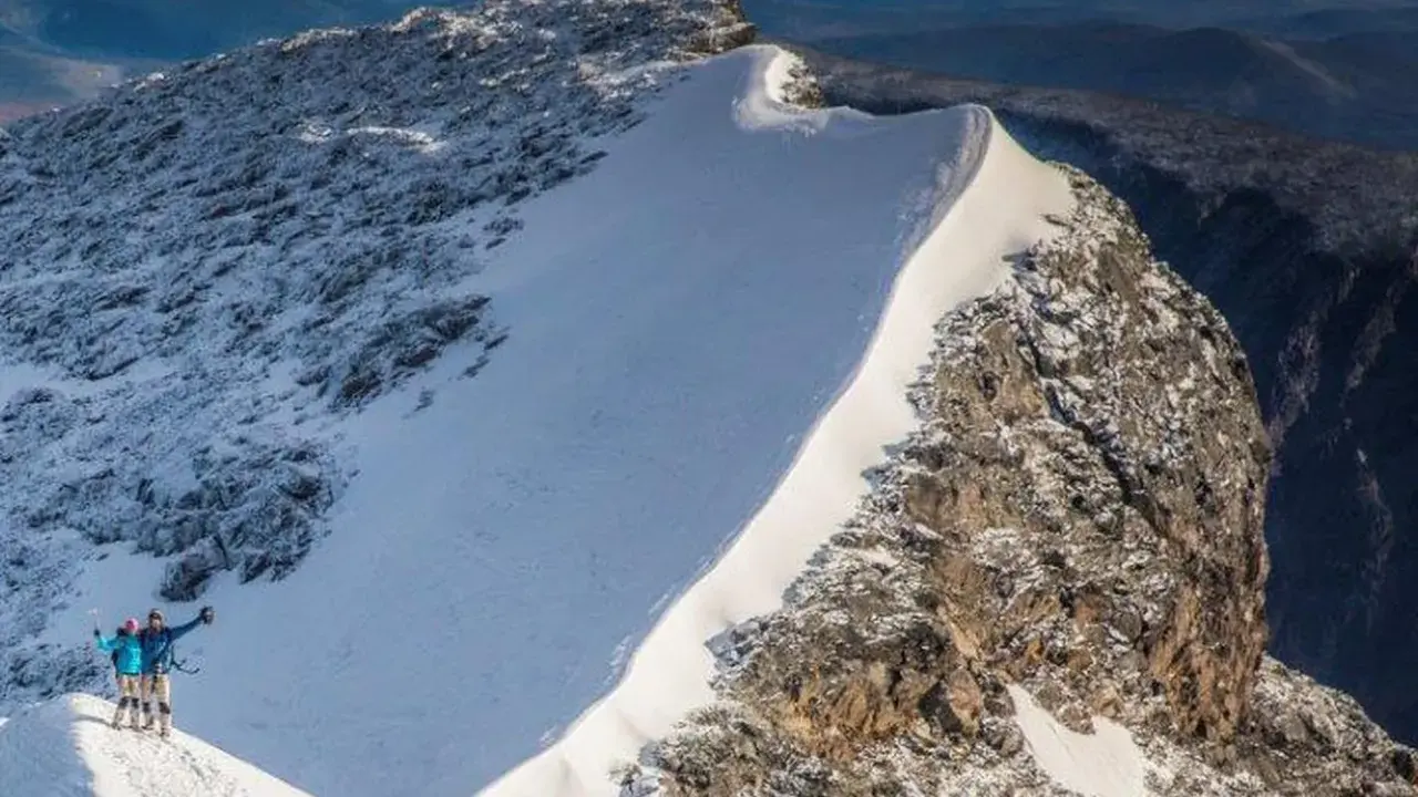 Två personer firar på toppen efter att ha lyckats bestiga Kebnekaise. Snö och sten dominerar landskapet.
