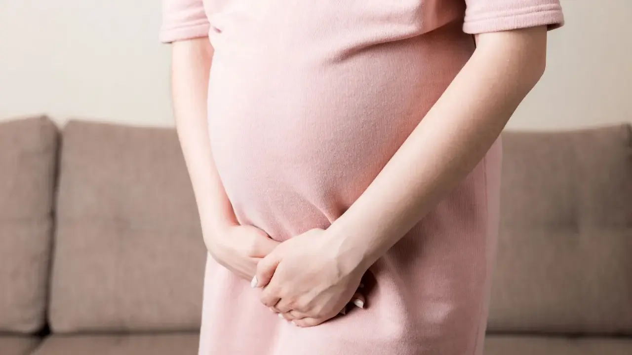 Kobieta w ciąży w różowej sukience trzyma ręce na brzuchu, doświadczając dyskomfortu związanego z nietrzymaniem moczu w ciąży.