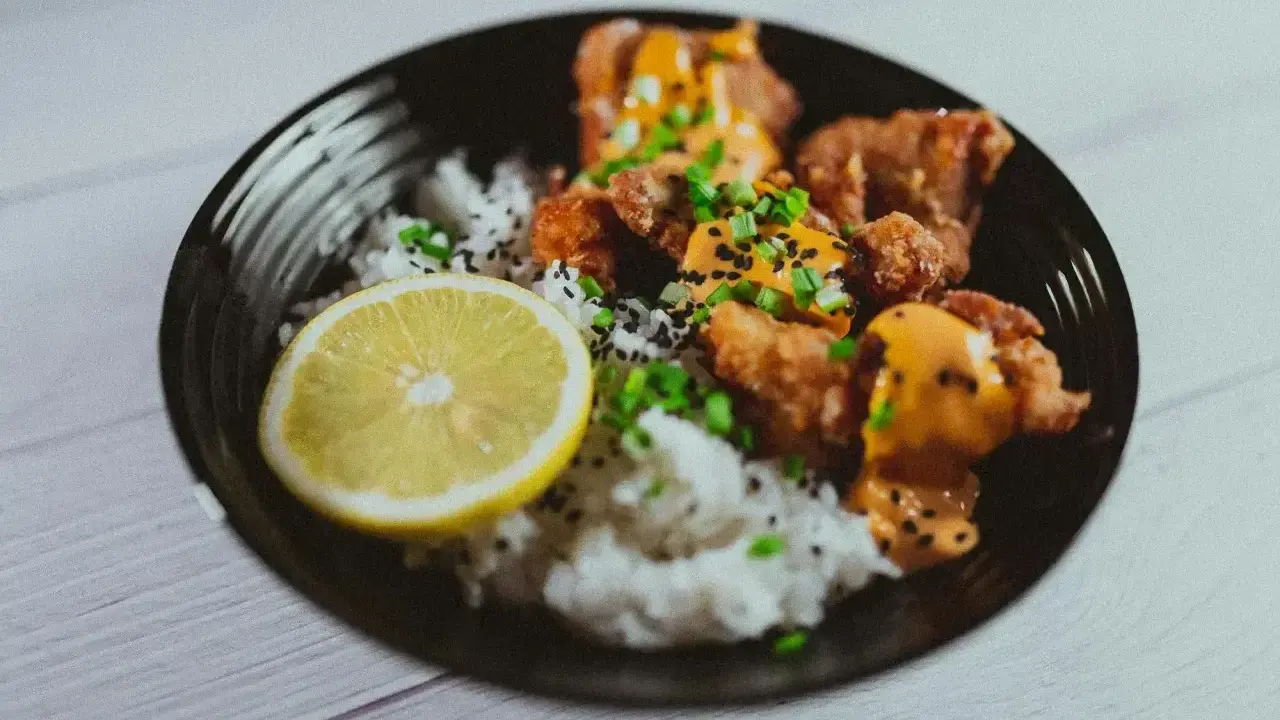 Chrupiące karaage z ryżem, posypane sezamem i szczypiorkiem, podane z plasterkiem cytryny.