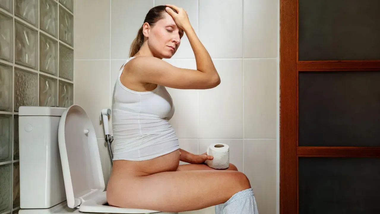 Donna incinta sul water, con la mano sulla fronte, preoccupata per la cacca in gravidanza.