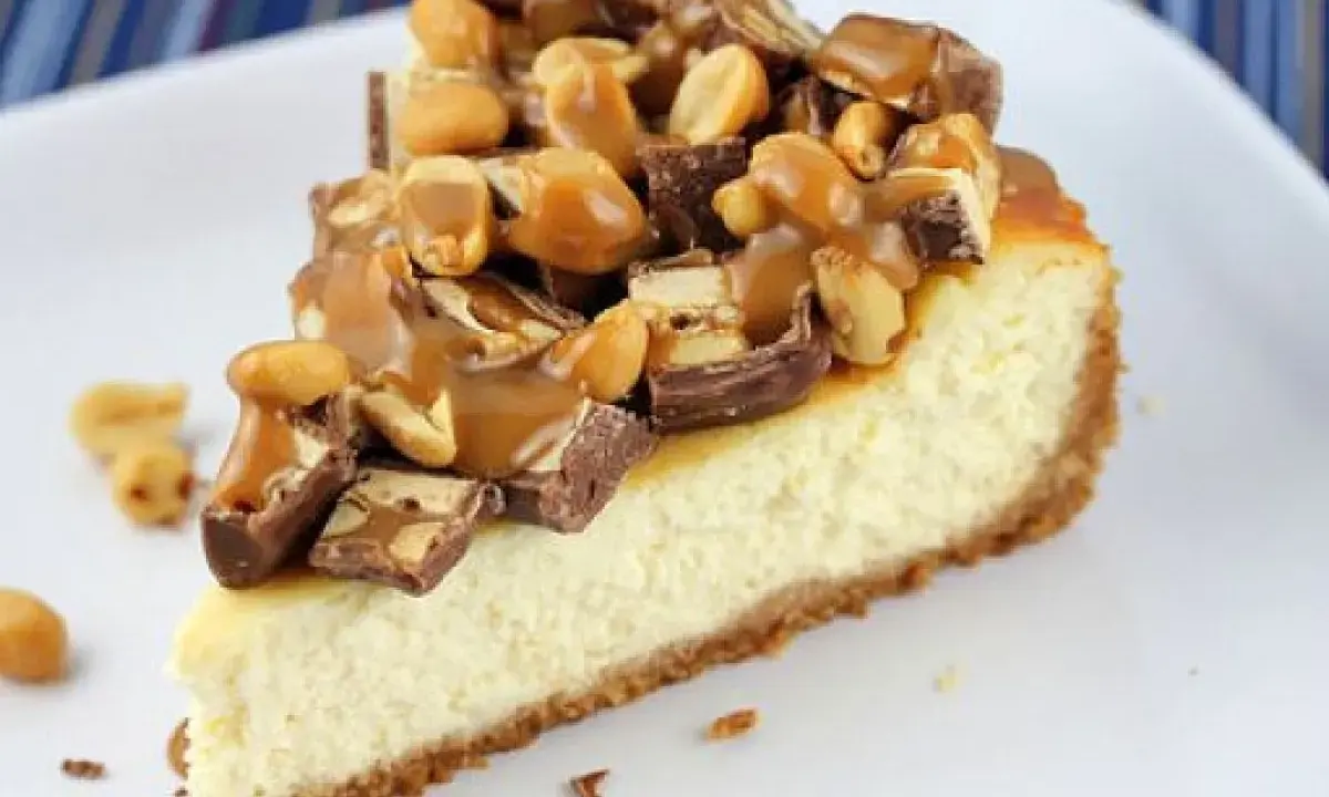 Kawałek sernika snickers z polewą karmelową i orzeszkami ziemnymi.