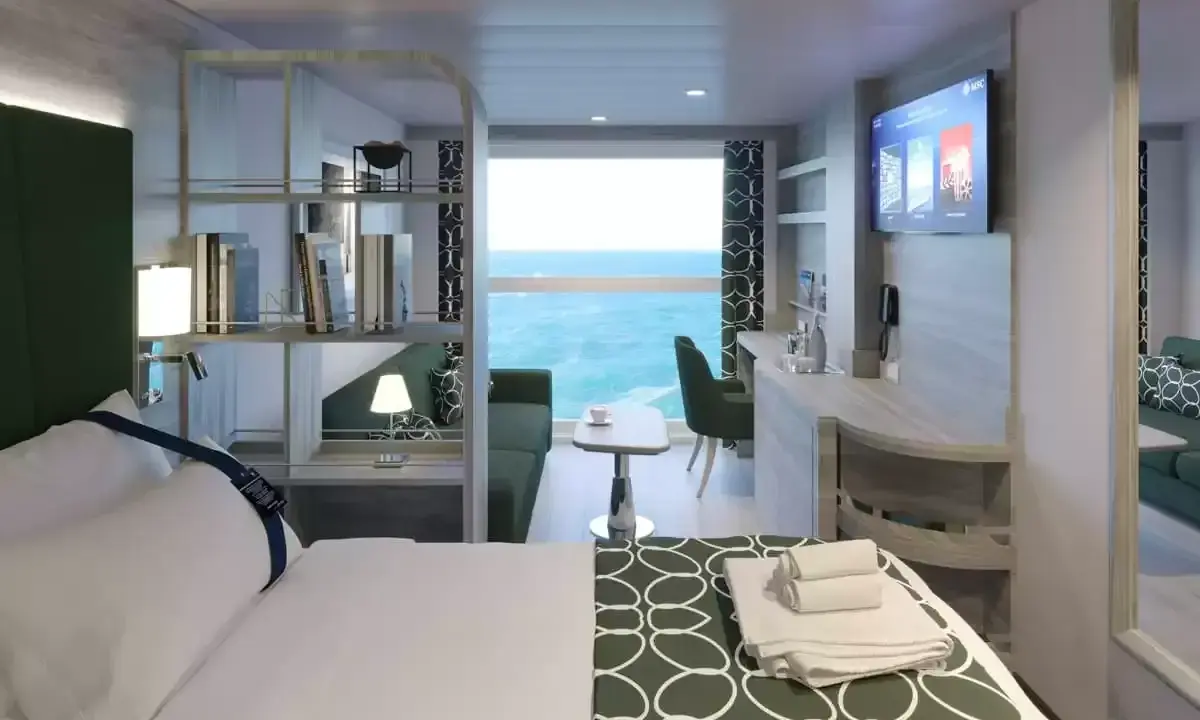 Interno cabina MSC World Europa: letto, divano, scrivania e vista mare.