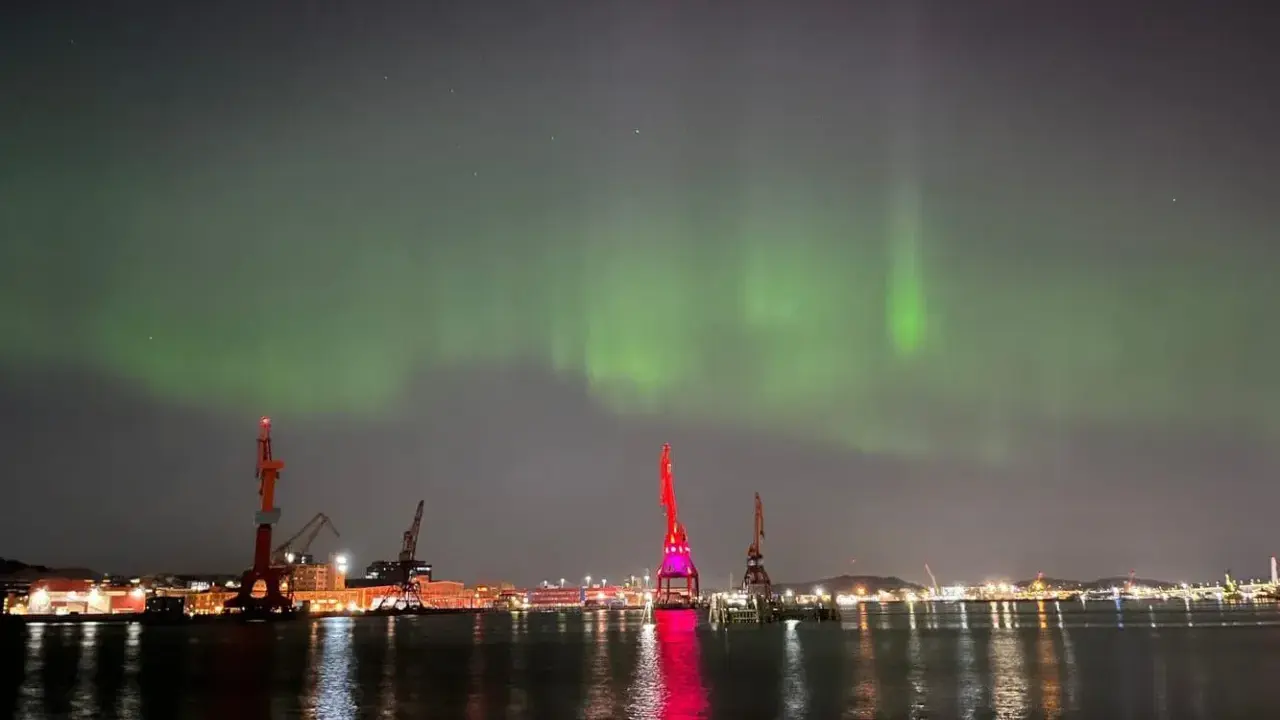 Norrsken över Göteborgs hamn. Kranar lyser upp natten medan himlen dansar i grönt.