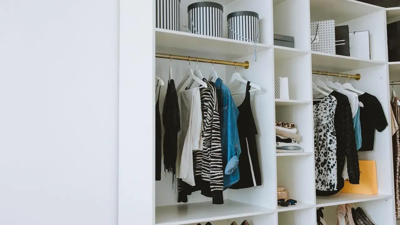 Un armario organizado con ropa colgada y doblada, cajas a rayas y bolsas de compras. Una guía visual de como organizar un armario de forma elegante.
