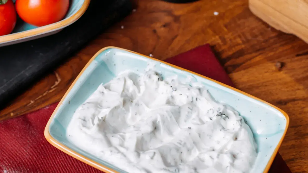 Sauce roquefort crémeuse et onctueuse, parsemée d'herbes vertes, dans un plat bleu clair. Parfait pour accompagner vos plats.