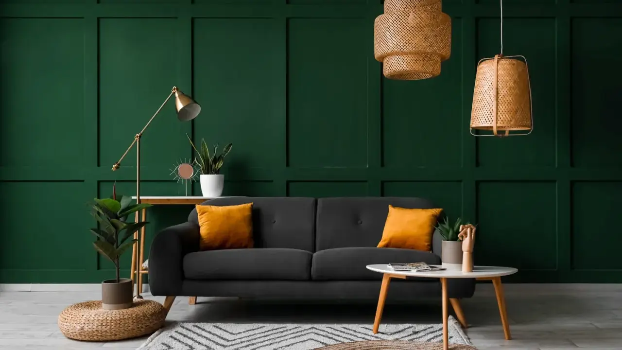 Canapé gris avec coussins orange vif sur fond vert foncé. Le jaune moutarde est une couleur qui va avec le vert foncé, créant un contraste chaleureux.