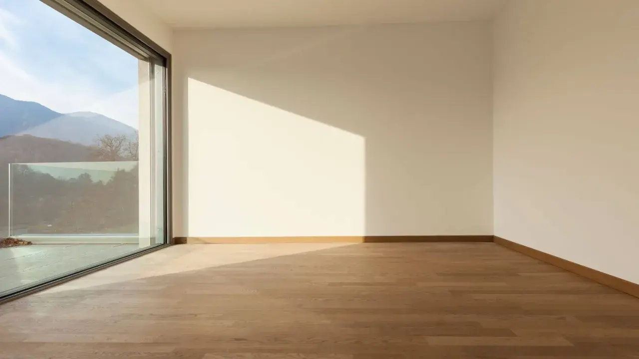 Habitación vacía con suelo de madera y gran ventanal de cristal planitherm que ofrece vistas a montañas.
