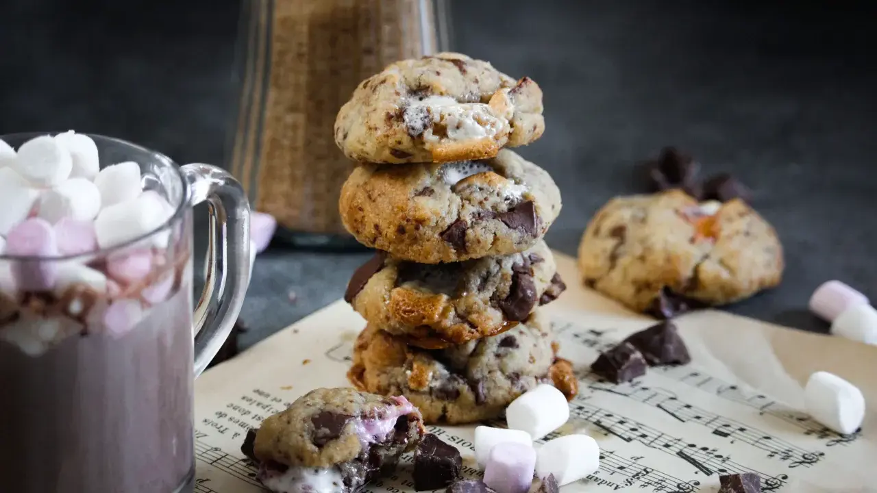 Un cookie chamallow fondant, empilé avec d'autres, à côté d'une tasse de chocolat chaud garnie de guimauves.