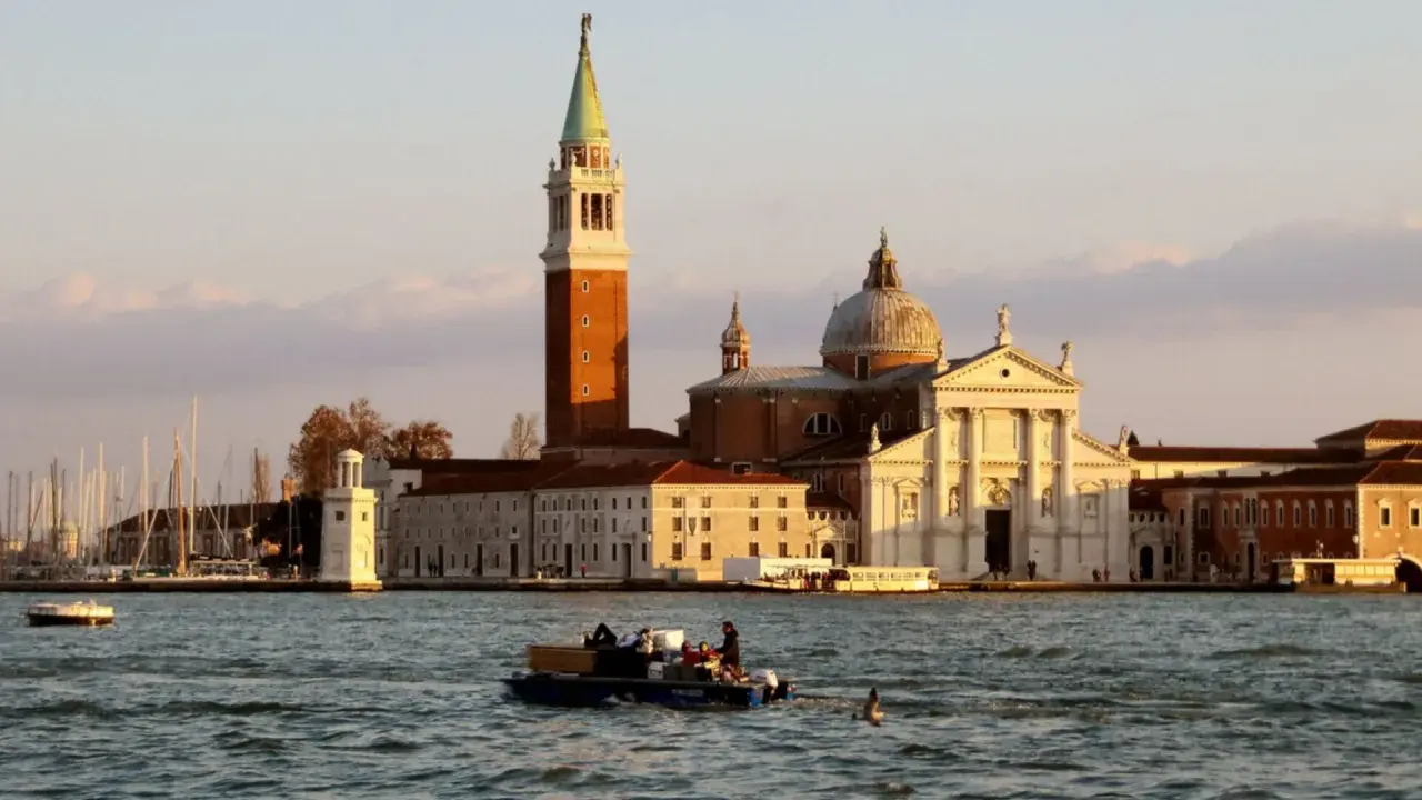 Le campanile et l'église de San Giorgio Maggiore à Venise se reflètent sur l'eau. Un bateau transporte des passagers.