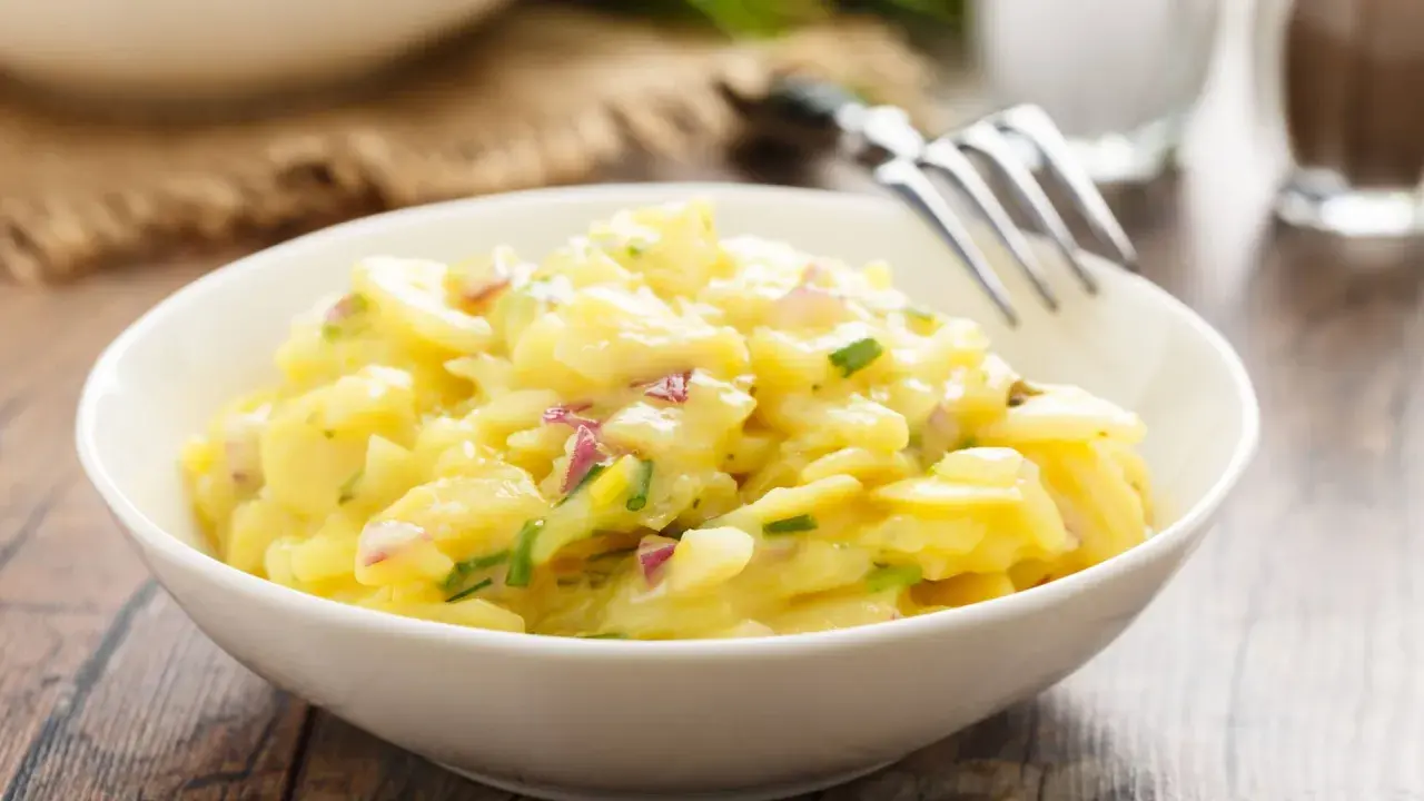 Schüssel mit cremigem Kartoffelsalat, garniert mit roten Zwiebeln und Schnittlauch. Ein köstliches Rezept für Kartoffelsalat!