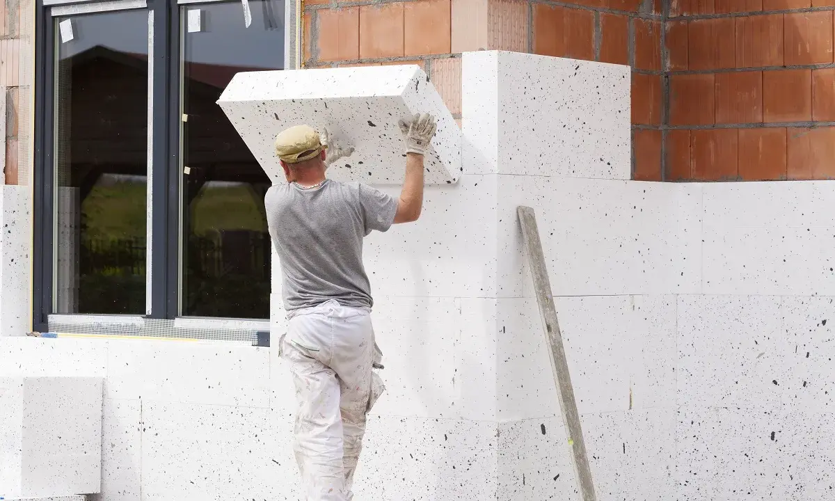 Budowlaniec montuje płyty ze styropianu grafitowego na elewacji. To dobry wybór, jaki styropian na elewację dla lepszej izolacji.