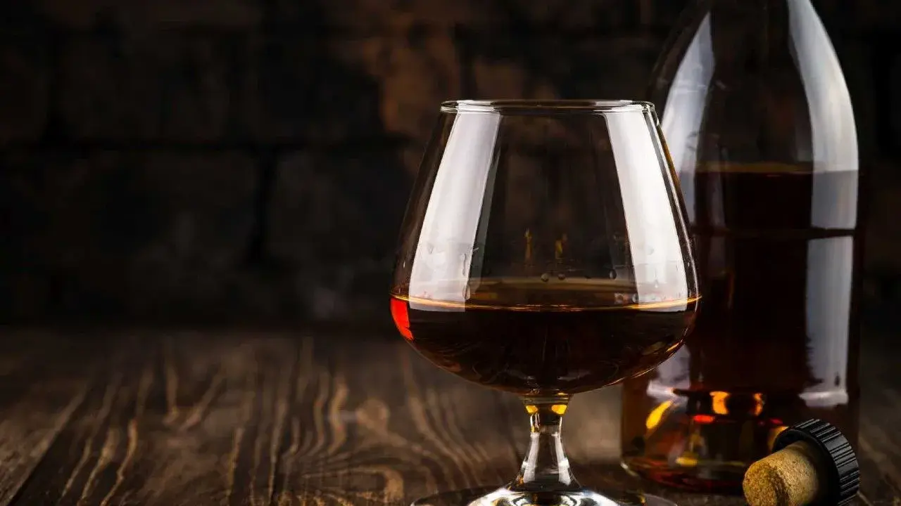 Kieliszek brandy obok butelki i korka na drewnianym stole.