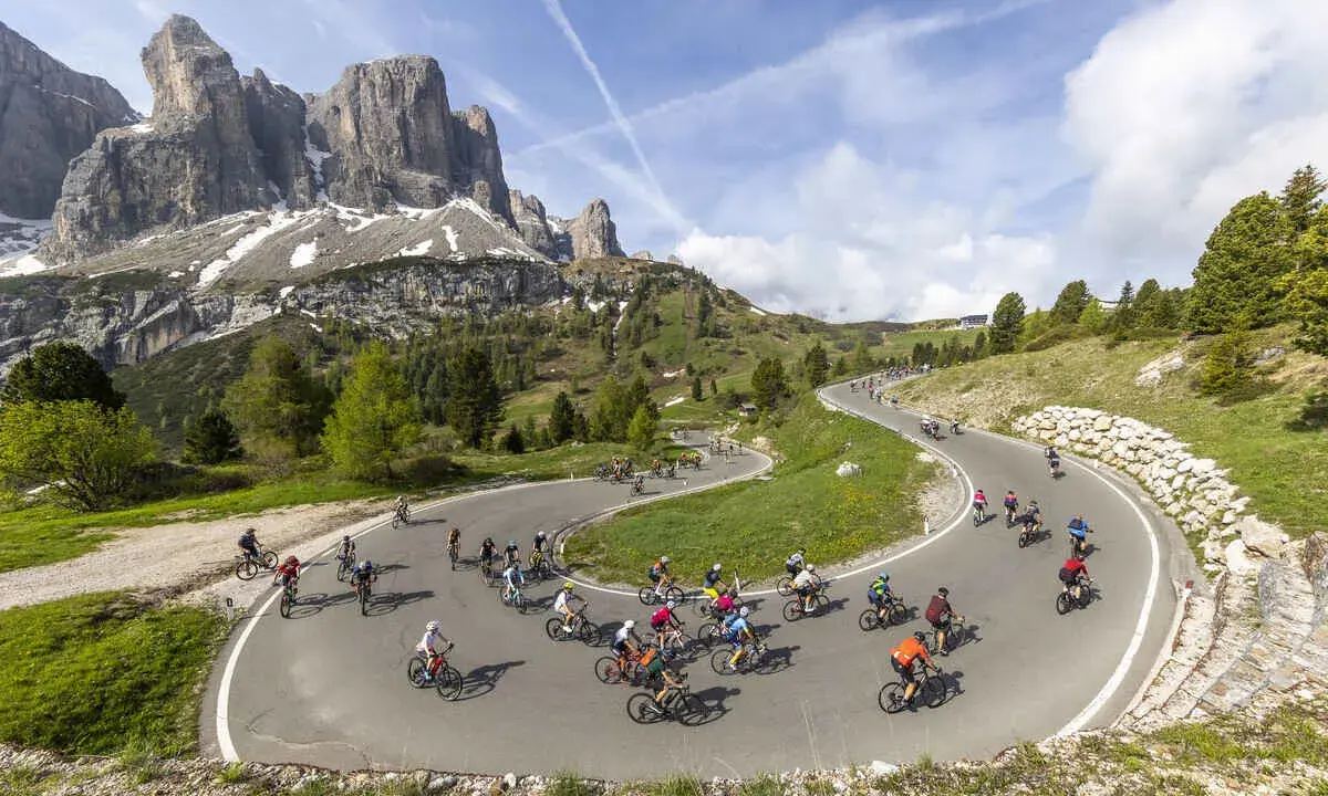 Ciclisti affrontano tornanti in una spettacolare salita alpe d'Huez, con maestose montagne sullo sfondo.