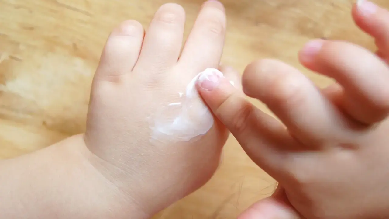 Mani di bambino applicano crema, un gesto che aiuta a contrastare la pelle atopica, alleviando secchezza e prurito.