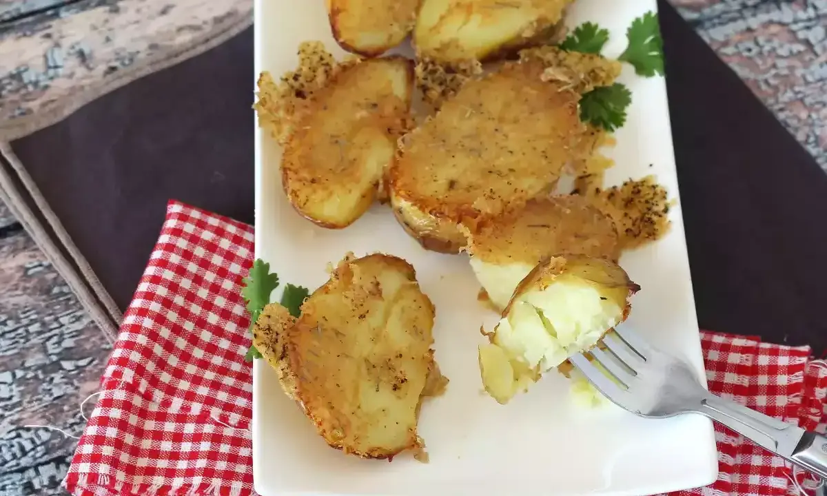 Krispiga, gyllene bitar av confiterad potatis, perfekt tillagade och serverade på en vit tallrik med en gaffel som visar den mjuka insidan.