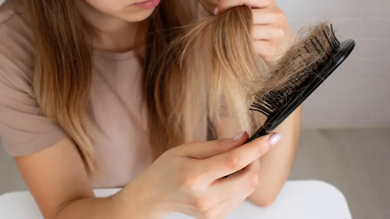 Donna preoccupata guarda i capelli persi sul pettine, chiedendosi perché perdo capelli.