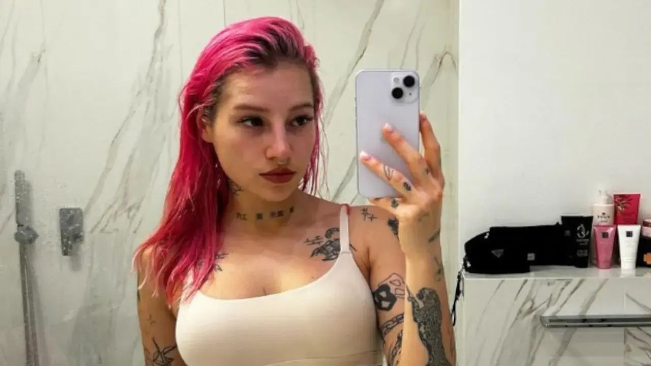 Młoda Leosia z kolorowymi włosami i licznymi tatuażami na ciele robi sobie selfie w łazience.