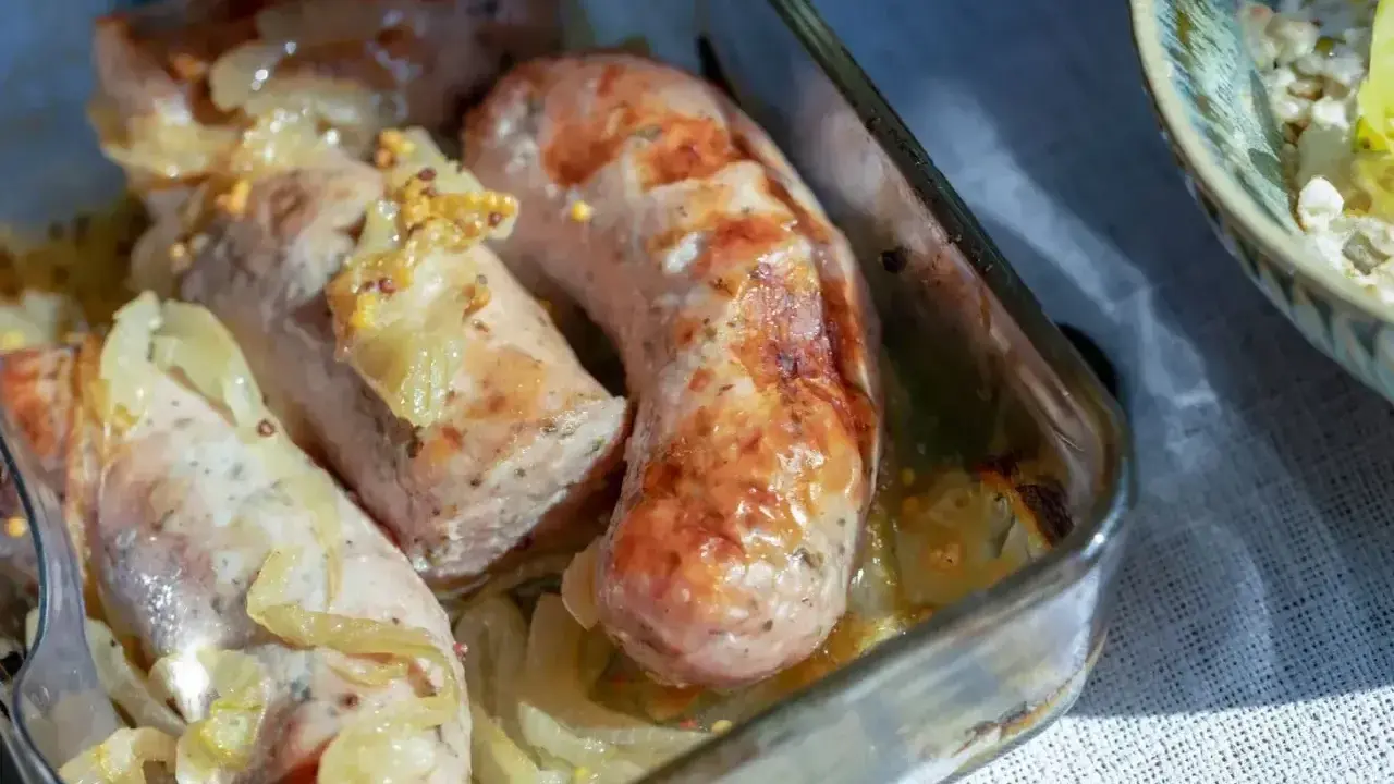 Aromatyczna, pieczona biała kiełbasa z cebulką i musztardą w szklanym naczyniu.