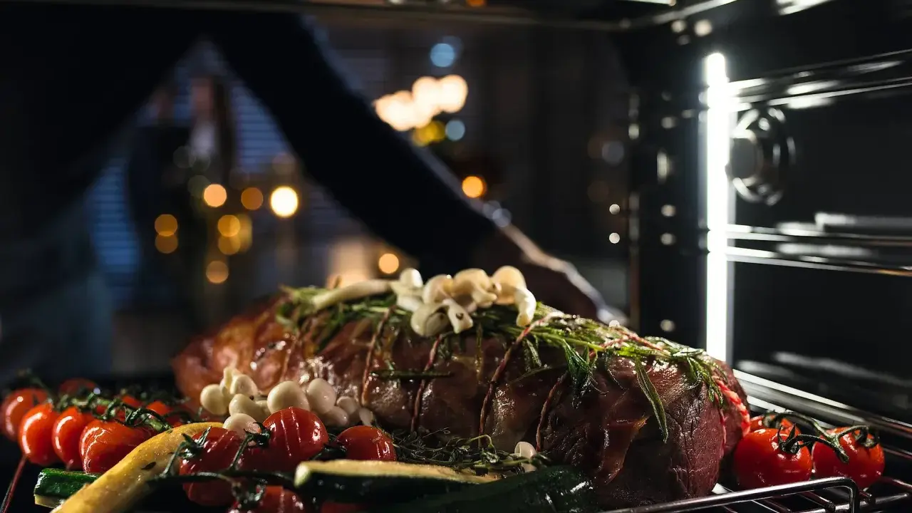 Ein Braten mit Kräutern, Knoblauch, Tomaten und Zucchini wird in den Ofen geschoben. So wird ein Dialoggarer zum Leben erweckt.
