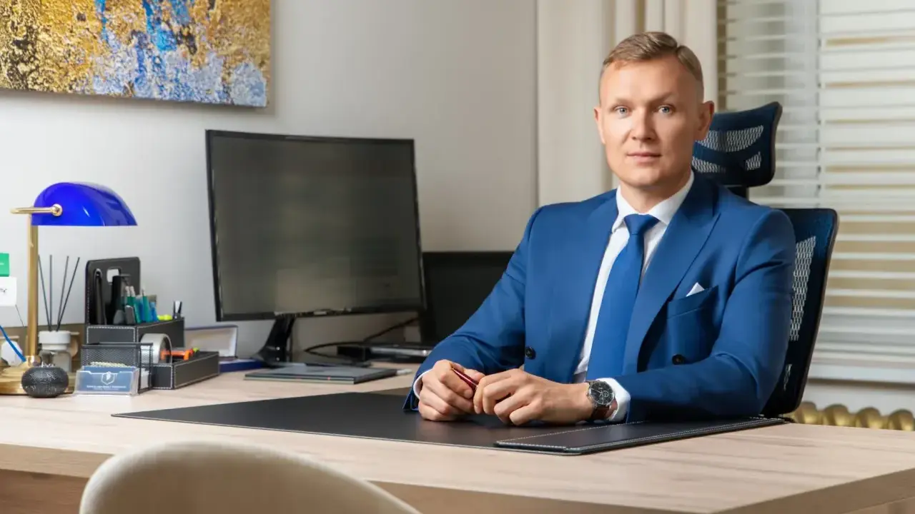 Mężczyzna w niebieskim garniturze siedzi przy biurku w nowoczesnym biurze.