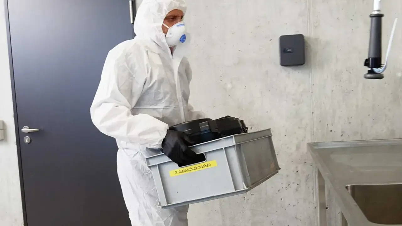 Hombre con traje blanco y mascarilla, lleva caja con equipo de protección obligatoria de vías respiratorias.